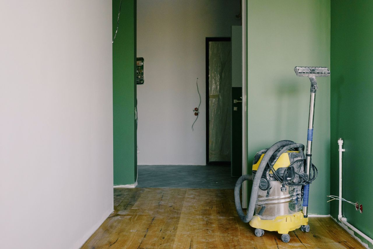 Industrial vacuum cleaner set on a dirty parquet floor in a room with green walls and a doorway inside a spacious apartment during renovation work